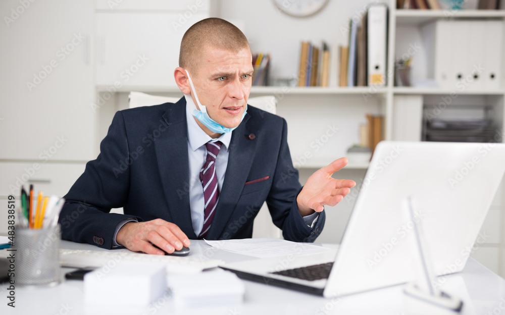 Confident head of the company in a protective mask, working in the office during a pandemic, conducts online ..negotiations with business partners on a laptop, discussing current business issues
