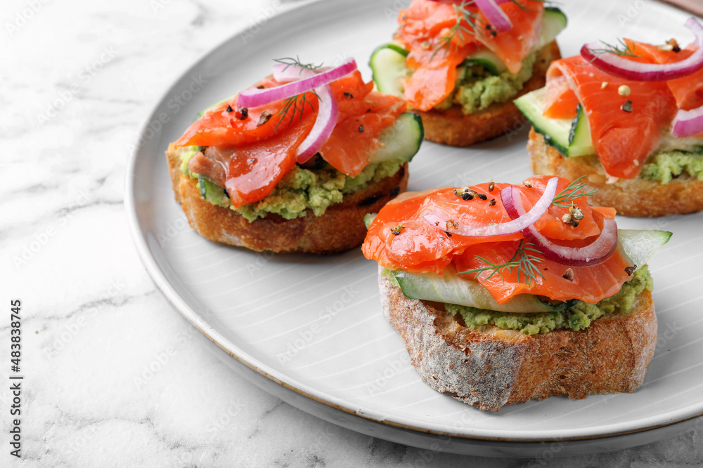 Delicious sandwiches with salmon, avocado, cucumber and onion on white marble table, closeup