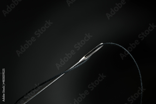 Sewing needle with black thread on dark background, closeup photo