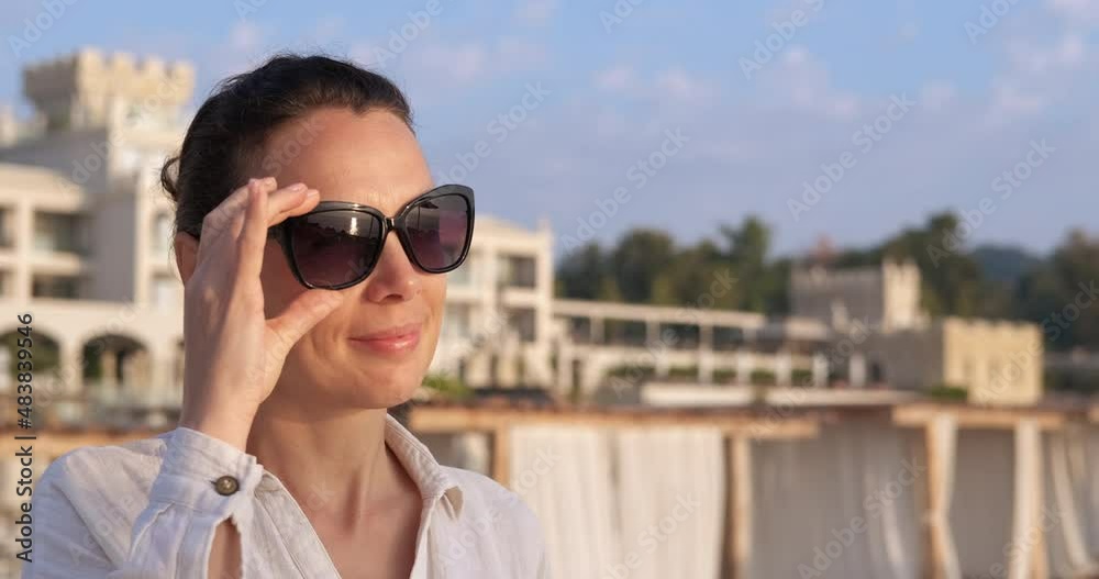 Woman standing on rocky shore. A woman in sunglasses stand in the sun against tourist hotel in summer. Woman standing on rocky shore. A woman in sunglasses stand in the sun against tourist hotel in summer.