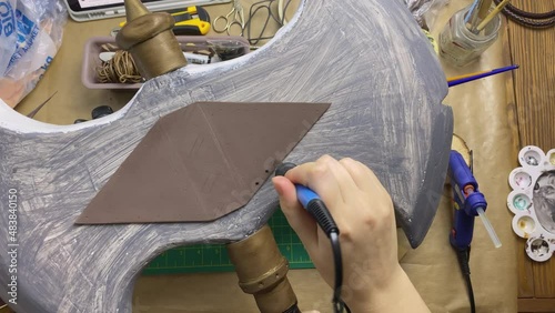 Person's hands make small holes in hatchet made of eva foam and styrofoam. Decorating with soldering iron. Celtic axe for cosplayer festival.