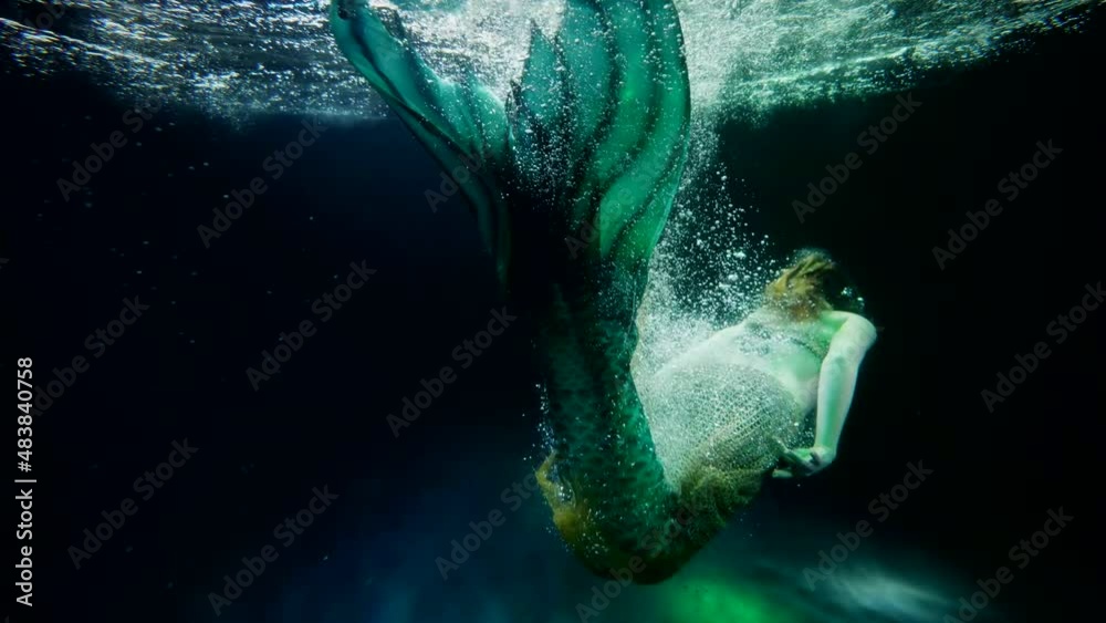 woman in suit of mermaid with fish tail is swimming inside sea depth, slow motion shot
