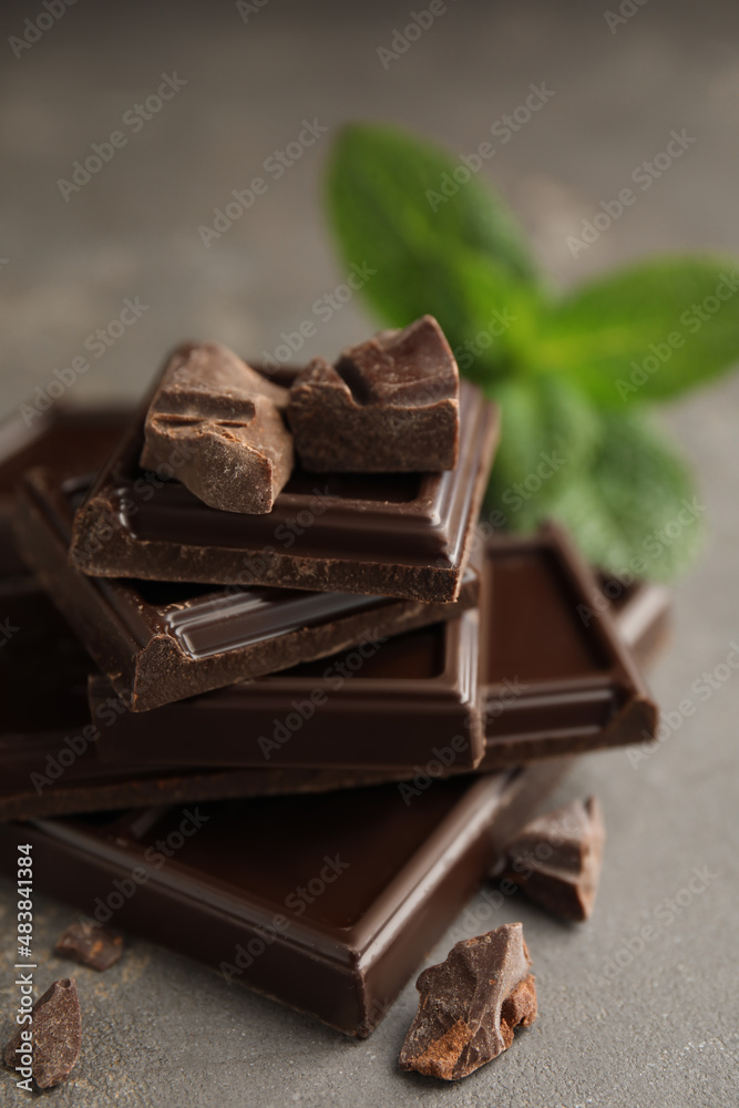 Tasty dark chocolate pieces with mint on grey table, closeup Tasty dark chocolate pieces with mint on grey table, closeup