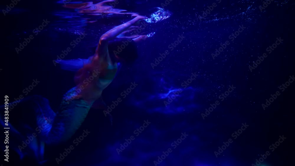 playful and fascinating mermaid is swimming in depth of sea, dark blue water of ocean or river