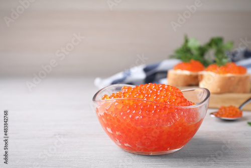 Glass bowl with delicious red caviar on white wooden table. Space for text