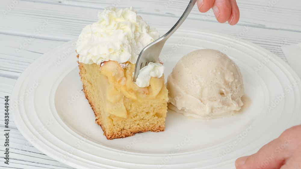 Slice of fresh baked apple cake with biscuit base and sliced apples and whipped cream topping served with vanilla ice cream close up on a plate Slice of fresh baked apple cake with biscuit base and sliced apples and whipped cream topping served with vanilla ice cream close up on a plate