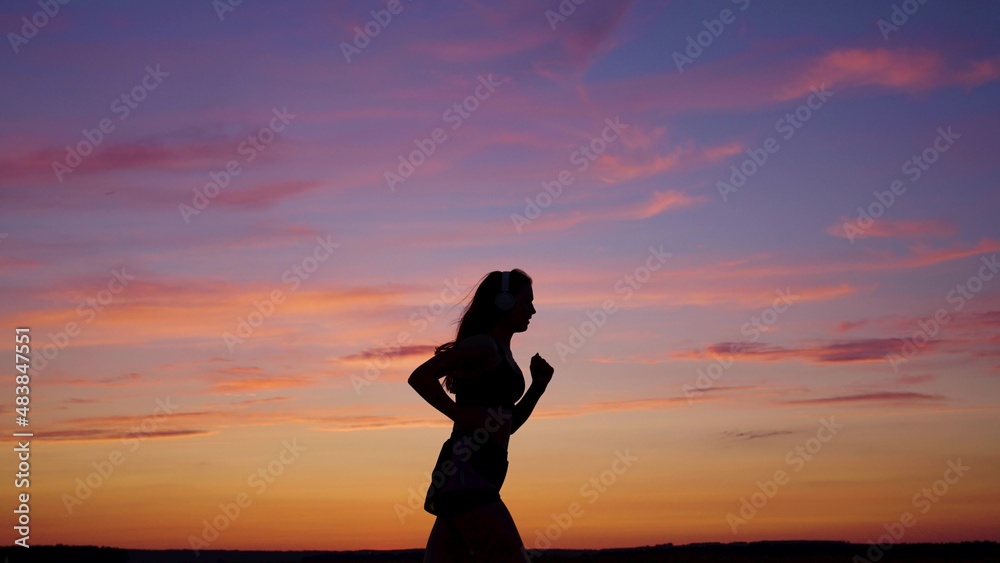 Silhouette of free young woman runs in summer in park at sunset, listens to music on headphones. Training jogging. Healthy jogging and outdoor exercise. Listen to music without Internet, play sports