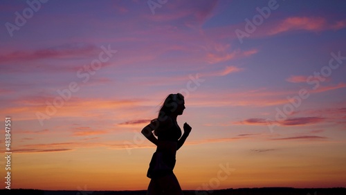 Silhouette of free young woman runs in summer in park at sunset  listens to music on headphones. Training jogging. Healthy jogging and outdoor exercise. Listen to music without Internet  play sports