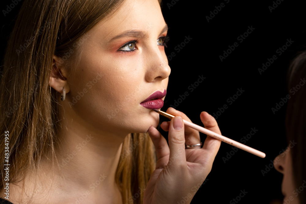 Makeup artist applies red lipstick on a beautiful woman face. Hand of make-up master, painting lips of young beauty model girl. Make up in process. Makeup artist applies red lipstick on a beautiful woman face. Hand of make-up master, painting lips of young beauty model girl. Make up in process.