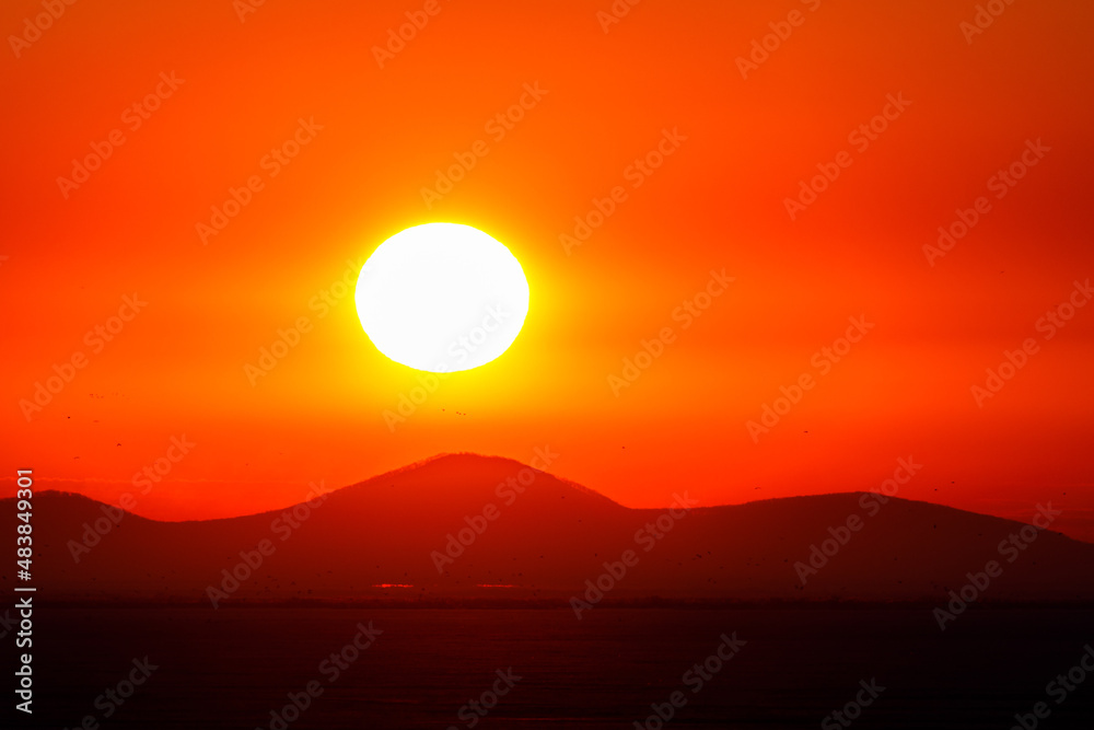 Obraz premium The bright sun sets on a low hill. Colorful sunset on the Khanka lake in Primorsky Krai.