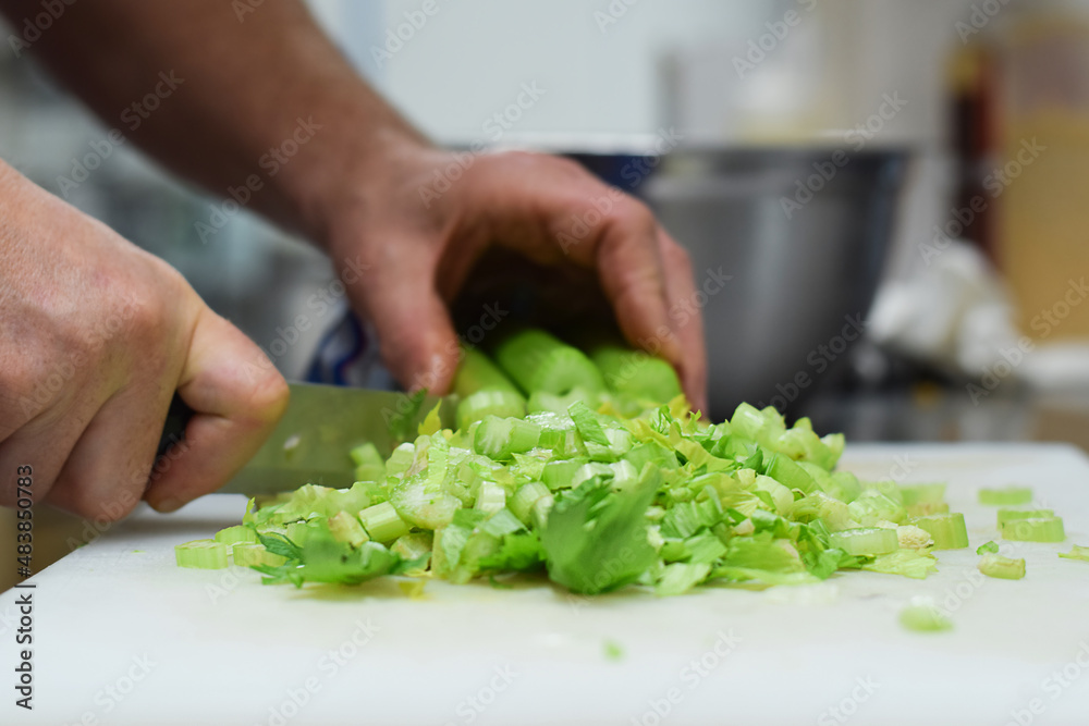 Restaurant kitchen employee cutting celery with knife
