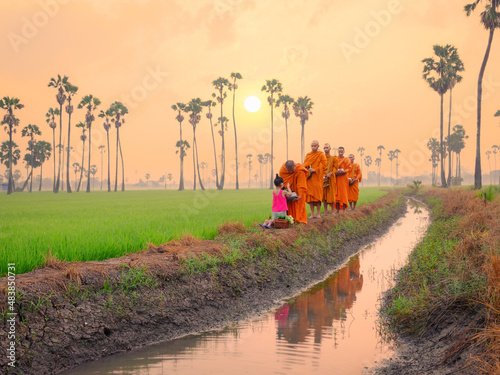 Fotografija Buddhist monk going about with alms bowl to receive food and girl giving food to