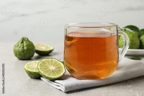Glass cup of tasty bergamot tea and fresh fruits on light grey table
