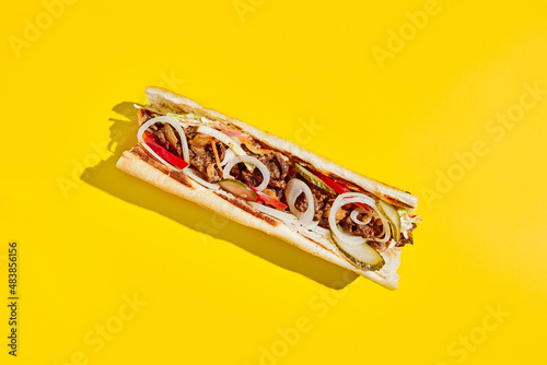 Beef cheesesteak with onion and pickle in minimal style. American fast food in yellow background with shadow. Philly steak sandwich trendy concept. Junk food in colour background.