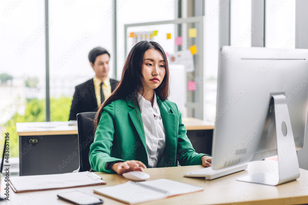 Beautiful confident asian businesswoman looking at desktop computer while sitting on office desk.Young creative coworkers business people working and planning Beautiful confident asian businesswoman looking at desktop computer while sitting on office desk.Young creative coworkers business people working and planning