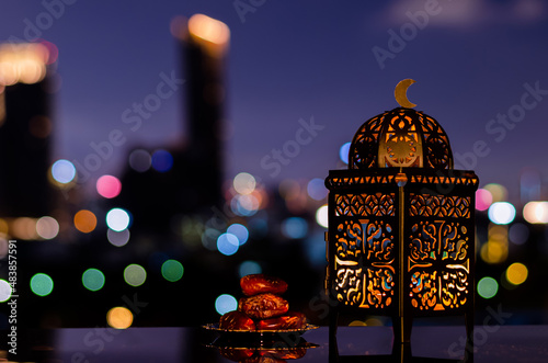 Lantern and small plate of dates fruit with night sky and city bokeh light background for the Muslim feast of the holy month of Ramadan Kareem.