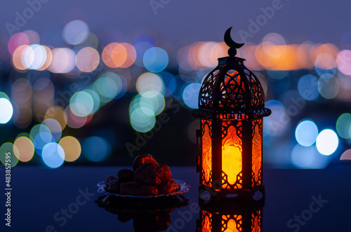 Selective focus of lantern that have moon symbol on top and small plate of dates fruit with city bokeh light background for the Muslim feast of the holy month of Ramadan Kareem. © baramyou0708
