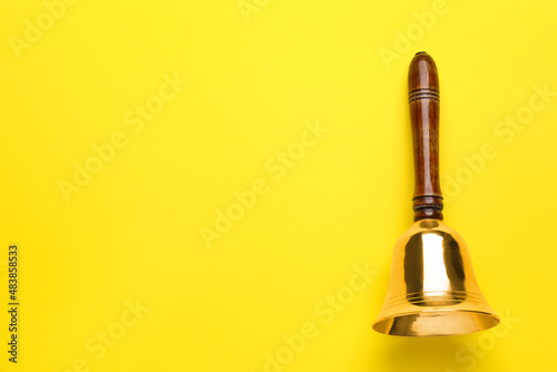 Golden school bell with wooden handle on yellow background, top view. Space for text photo