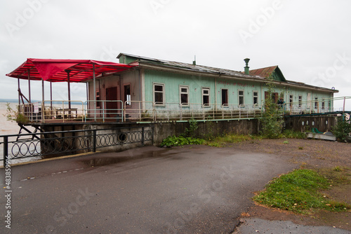 an abandoned cafe ship at the pier, an old wooden building on the water near the river, a bankrupt recreation center
