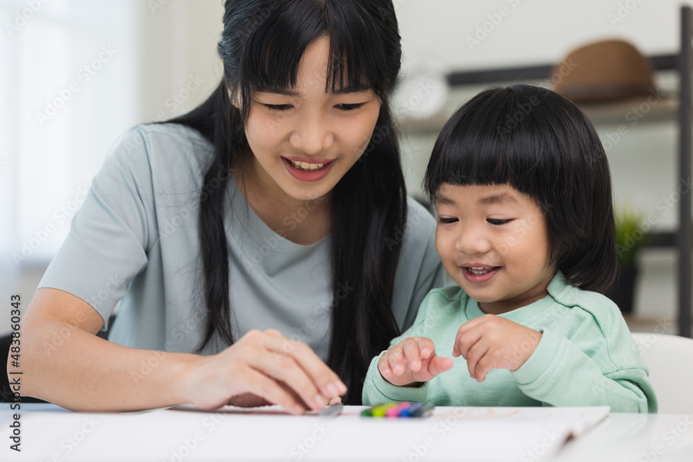 Happy asian boy painting with crayon and colored pencil with his mother in living room at home. Mom teaching son how to painting with crayon color on book or doing homework. family concept. Happy asian boy painting with crayon and colored pencil with his mother in living room at home. Mom teaching son how to painting with crayon color on book or doing homework. family concept.