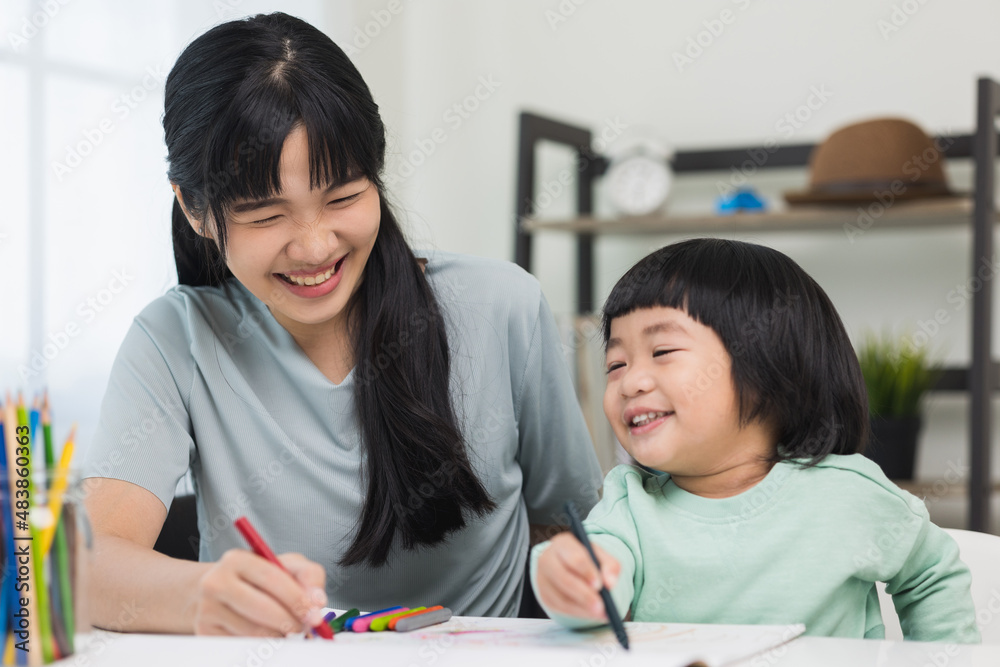 Happy asian boy painting with crayon and colored pencil with his mother in living room at home. Mom teaching son how to painting with crayon color on book or doing homework. family concept. Happy asian boy painting with crayon and colored pencil with his mother in living room at home. Mom teaching son how to painting with crayon color on book or doing homework. family concept.