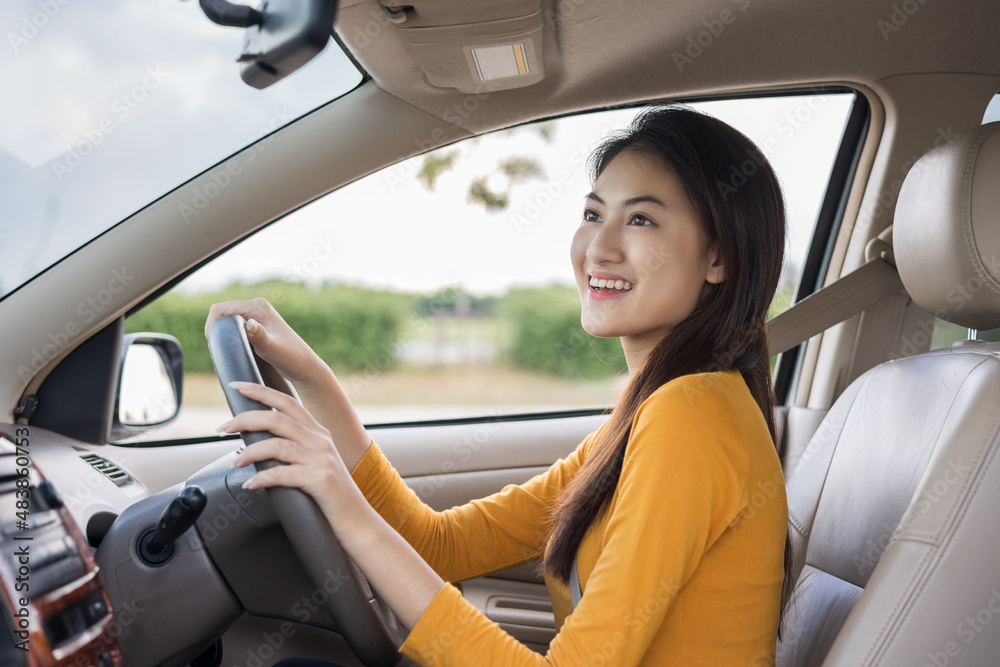 Naklejka premium Young beautiful asian women getting new car. she very happy and excited Look the rearview mirror while reversing the car. Smiling female driving vehicle on the road on a bright day