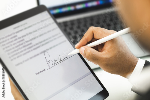 Close up businessman hand electronic Signature on Tablet by Stylus. Write business agreement of contract. Man signing contract on tablet. Business and technology concept. photo
