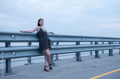 A girl with long hair in a black dress is standing near an empty road