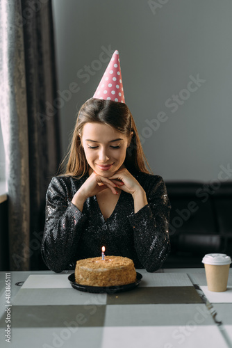 Happy young woman with candle on birthday cake at home. Close-up of a delicious cake on the table while a woman makes a birthday wish. Cheerful girl