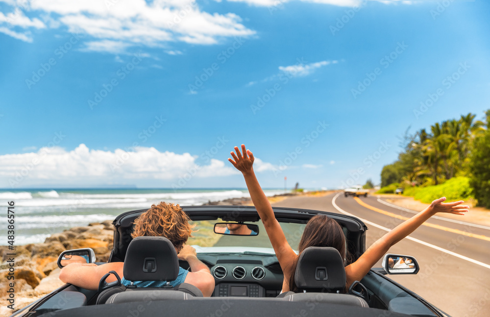 Road trip car holiday happy couple driving convertible car on summer travel Hawaii vacation. Woman with arms up having fun, young man driver - obrazy, fototapety, plakaty 