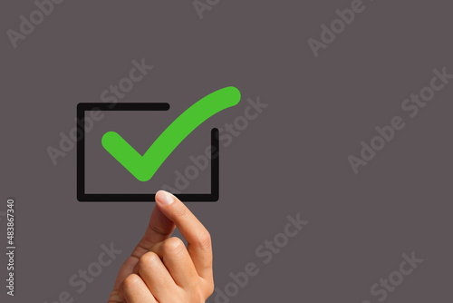 Fotografie Hand holding a green check mark symbol with a black border against a gray background
