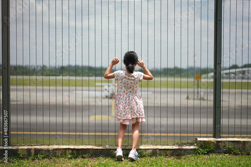 Little asian child looking at airport behind fence longing for travel