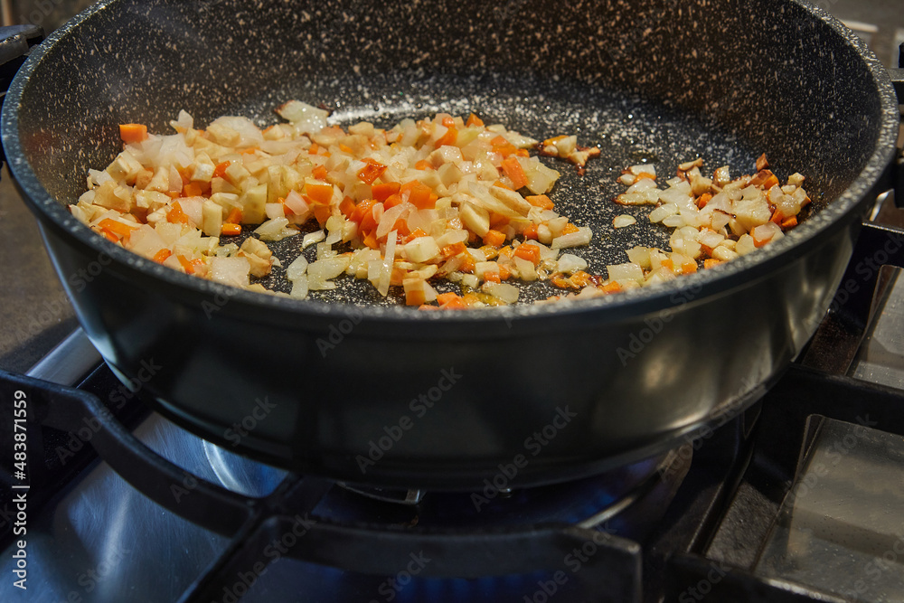 Onions and carrots are fried in pan on gas stove