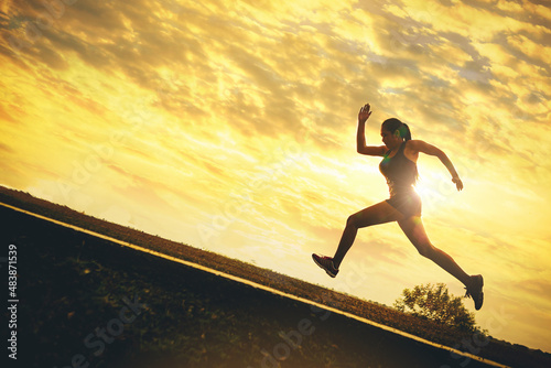 Silhouette of young woman running sprinting on road. Fit runner fitness runner during outdoor workout with sunset background. 