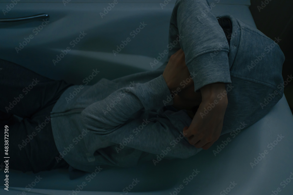 A young woman in a hood sits in the bathroom and covers her face with her hands. The concept of mental and psychological health, depression. A young woman in a hood sits in the bathroom and covers her face with her hands. The concept of mental and psychological health, depression.