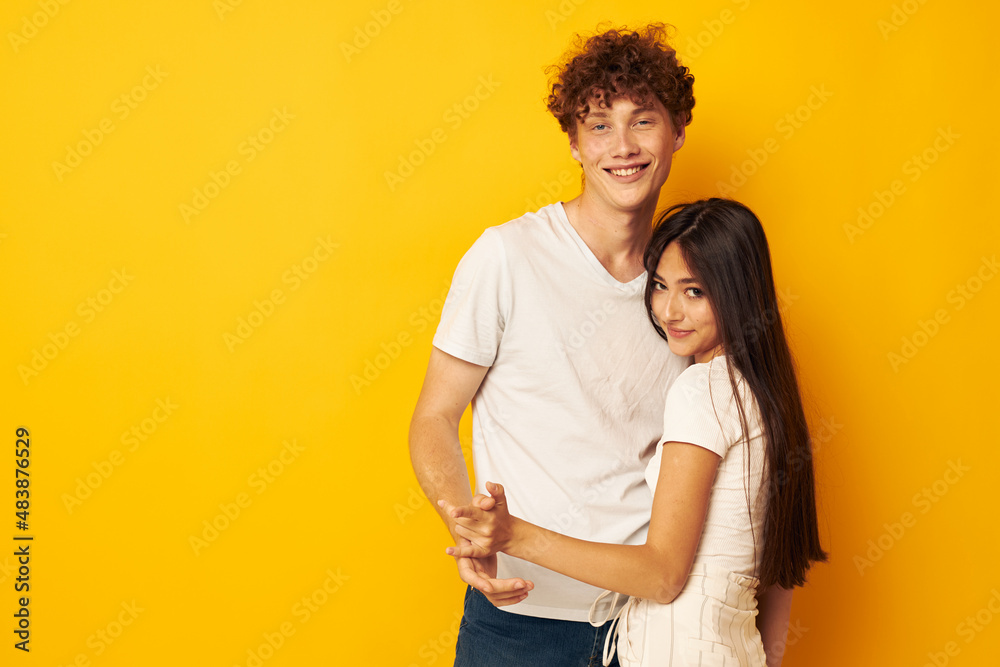 Naklejka premium portrait of a man and a woman stand hugging each other in white T-shirts yellow background unaltered