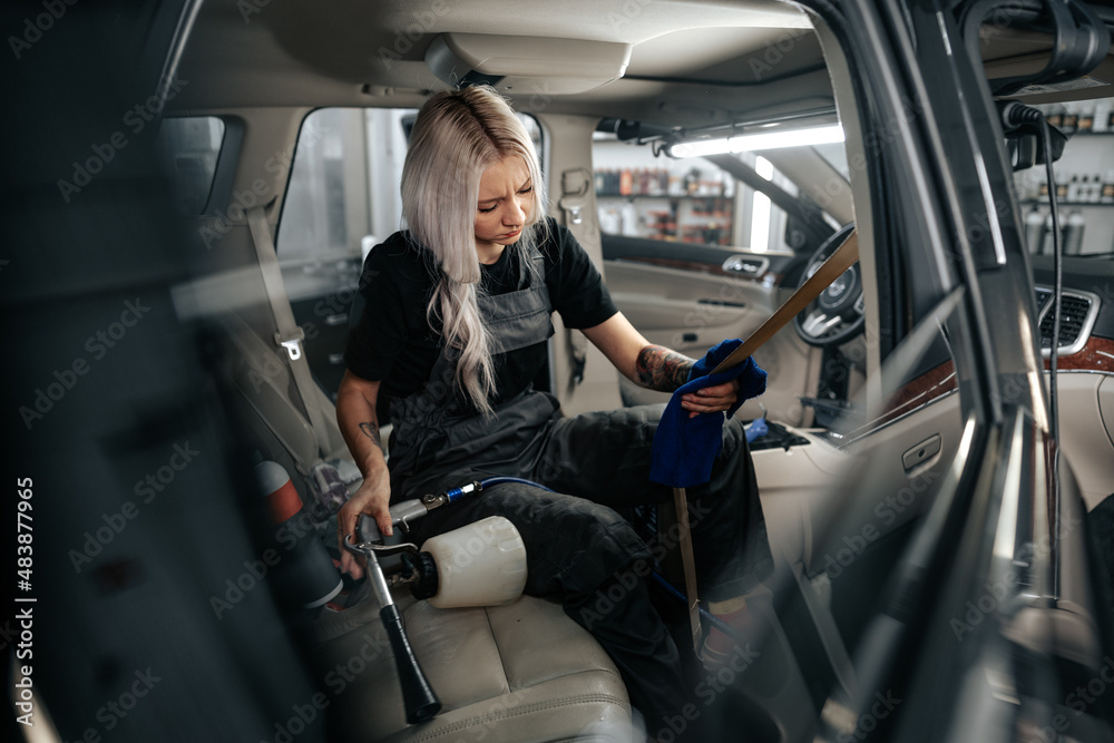 Woman cleaning car salon with polishing spray in car detailing service Woman cleaning car salon with polishing spray in car detailing service