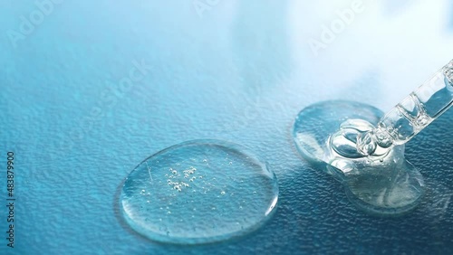 Hyaluronic acid flows down from a glass pipette on a blue background. Drops of transparent cosmetic product with bubbles. photo