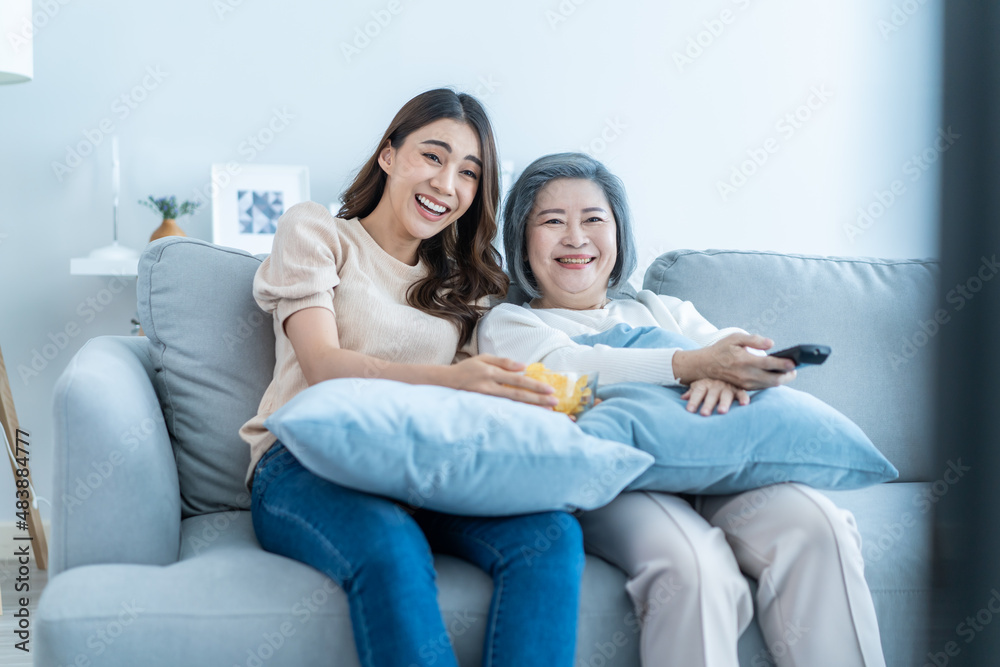 Asian senior mature woman and daughter sit on sofa watch funny movie. 