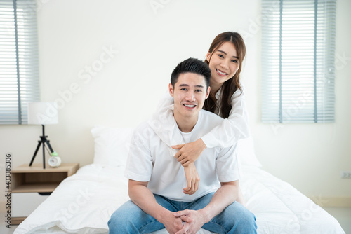 Portrait of Asian new marriage couple sit on bed and look at camera.