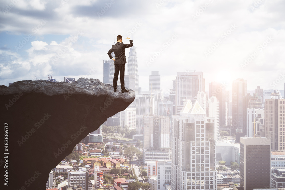 Attractive young european male on cliff edge looking into the distance on bright city background with daylight and mock up place. Future, success, leadership and career growth concept. Attractive young european male on cliff edge looking into the distance on bright city background with daylight and mock up place. Future, success, leadership and career growth concept.