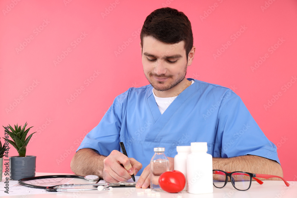 Doctor intern sits at workplace on pink background Doctor intern sits at workplace on pink background