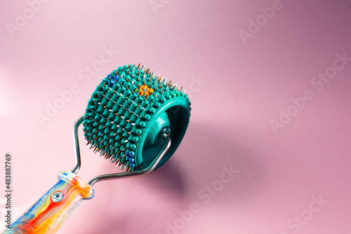 Roller Lyapko for massage and rehabilitation on a pink background. Device massager Lyapko with needles. Spiky roller with metal needles. 