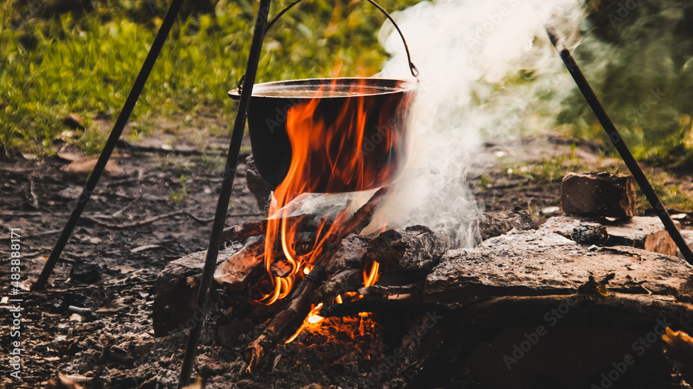 Cooking on an open fire in the field. A camp pot on a campfire close-up on a summer, clear day. Pot on fire with smoke close-up.Cauldron on fire. Cooking dish in a metal pot on an open fire. Cooking on an open fire in the field. A camp pot on a campfire close-up on a summer, clear day. Pot on fire with smoke close-up.Cauldron on fire. Cooking dish in a metal pot on an open fire.