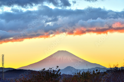 夕陽が山に沈みオレンジ色の光を富士山に照らす景色