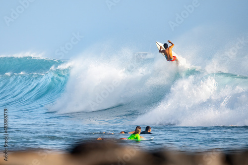 Surfer riding a barrel wave with air trick on a short board while other surfers look at him