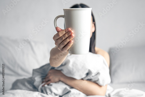 A woman holds a cup of coffee while lying in bed.