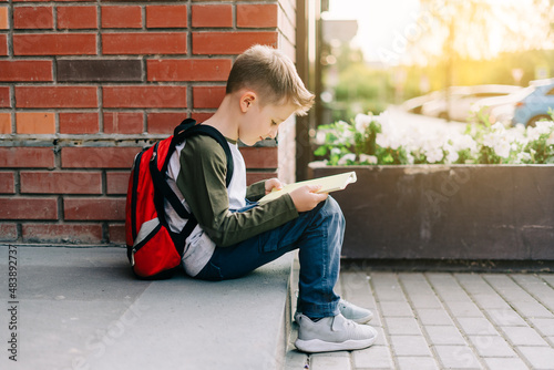 Back to school. Cute child with backpack, holding notepad and training books. School boy pupil with bag. Elementary school student going to classes. Kid sitting on stairs outdoors at brick wall.