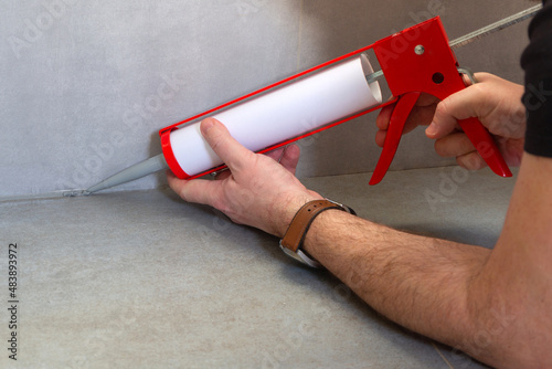 A plumber applies silicone sealant to the joining of ceramic tiles in the bathroom photo