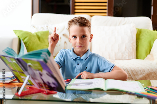 Caucasian school boy doing homework and Points the index finger up gesture